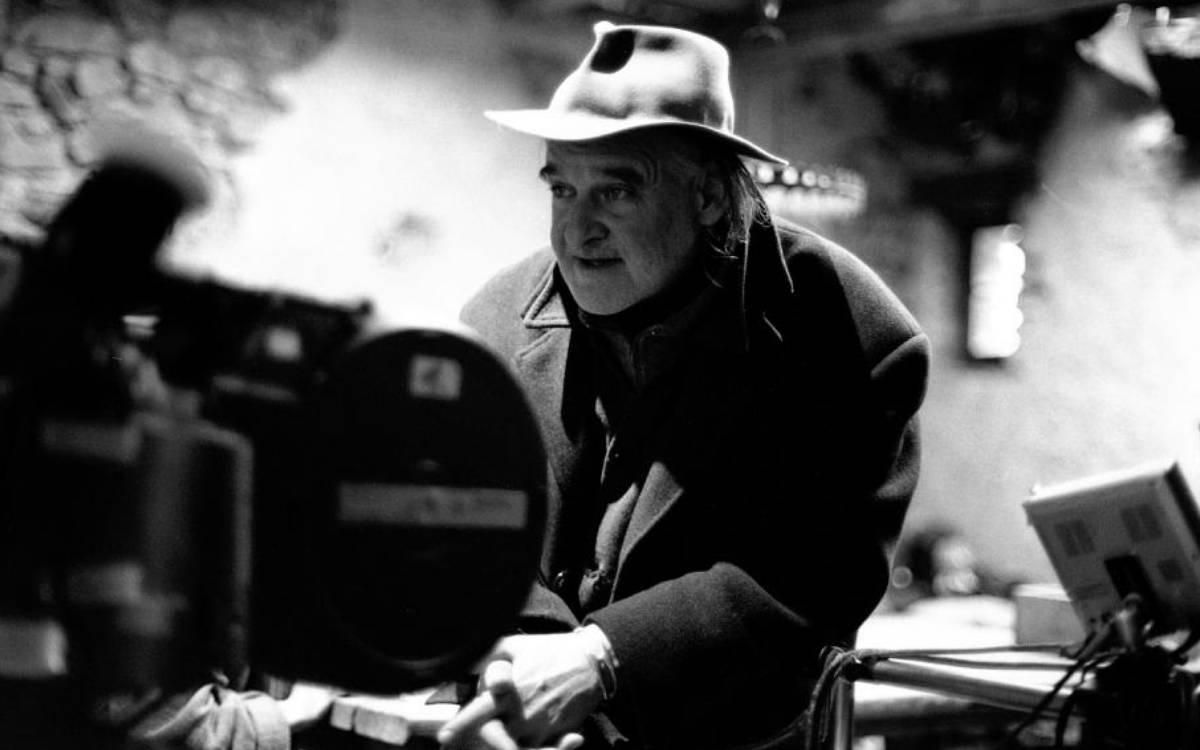Siyah beyaz bir fotoğrafta, Macar yönetmen Béla Tarr bir film setinde görülüyor. Tarr, üzerinde koyu renkli bir palto ve başında fötr bir şapka ile bir film kamerasının hemen arkasında durmaktadır. Ellerini önünde birleştirmiş, hafifçe yana doğru odaklanmış bir ifadeyle bakmaktadır. Arka plan bulanıktır ve iç mekan çekimini andıran loş bir aydınlatmaya sahiptir.